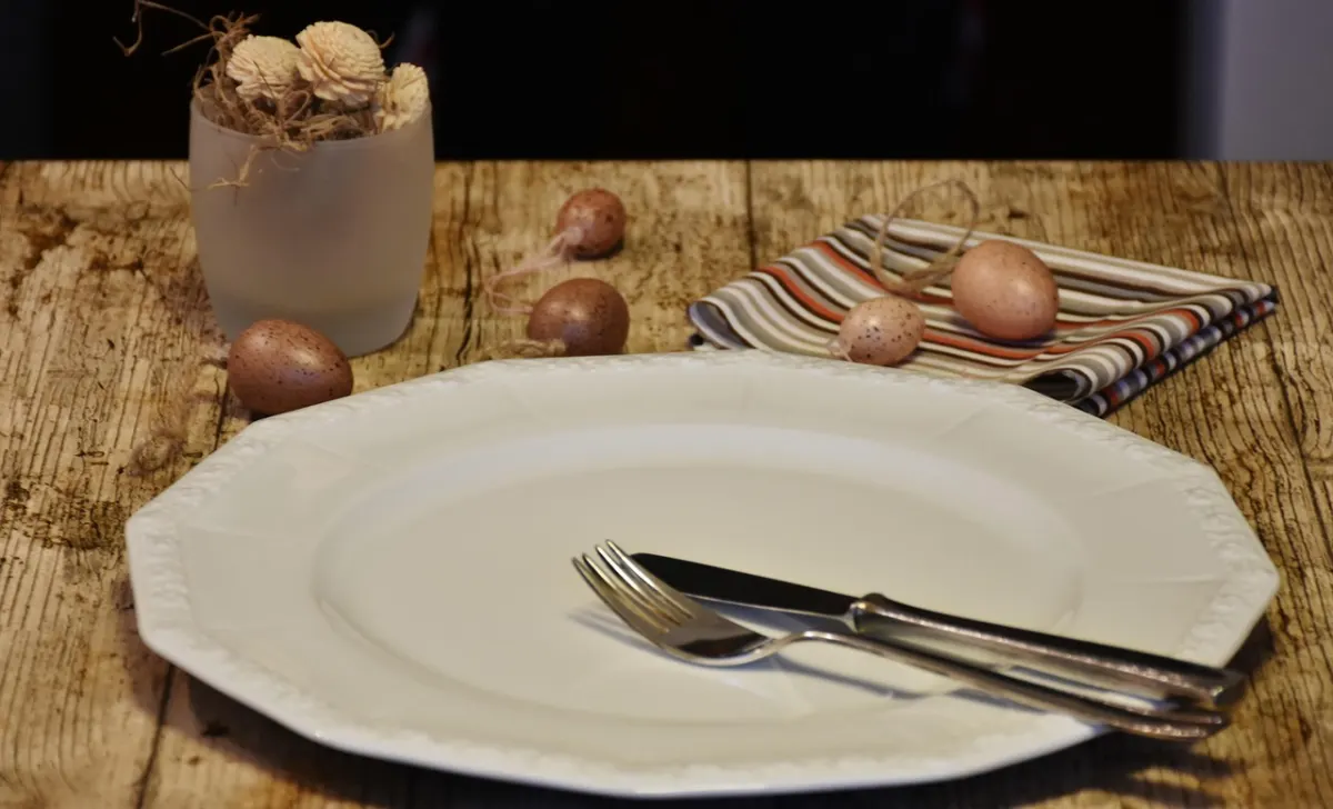 An empty plate with a knife and fork on a wooden table.