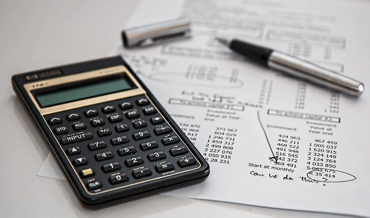 A calculator and financial paperwork on a desk with a pen.