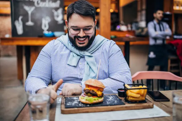 Man looking at a large burger and fries, representing the dietary challenges that individuals may face before considering weight loss surgery at Sleeve Clinic.